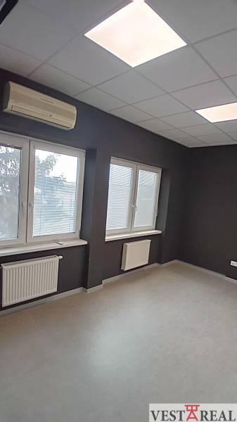 An office with windows, blinds, and air conditioning, equipped with a radiator and a floor with a wooden decor.