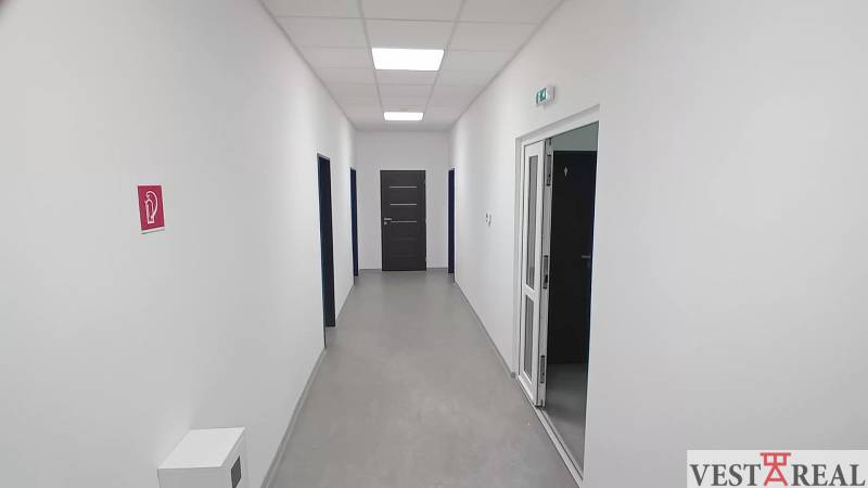 A narrow hallway in offices with white walls and a door at the end.