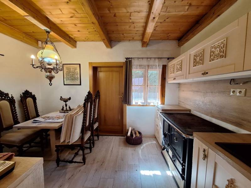 Rustic kitchen with wooden decor, decorative chairs, and a traditional stove in a cottage.