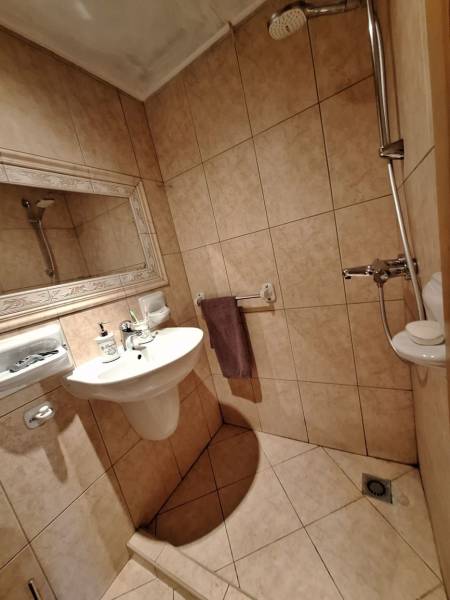 A bathroom in a cottage with tiles and a shower, equipped with a sink and a mirror.