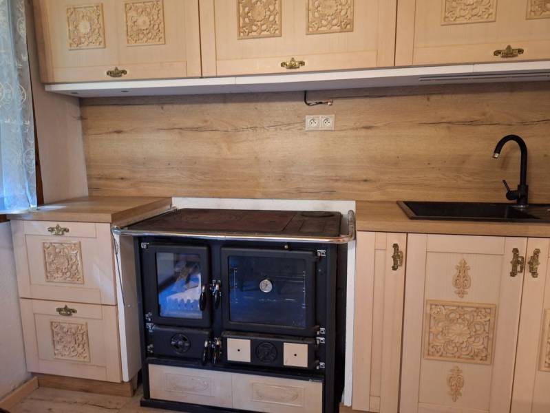 A kitchen unit with rustic cabinets, a black stove, and wooden paneling in a cabin.