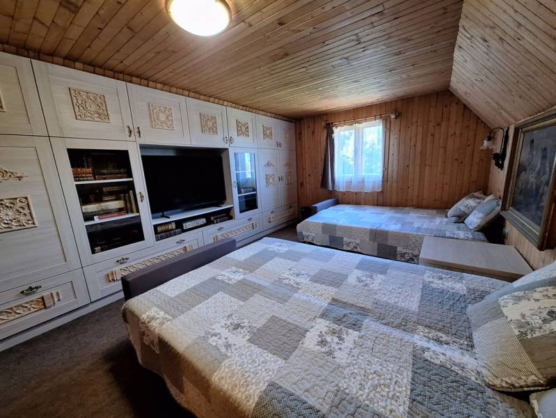 A cottage with a wooden decor floor, beds, wardrobes, and a window with a curtain.