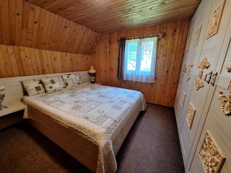 A bedroom in a cabin with wood decor, a comfortable bed, and a richly decorated wardrobe.