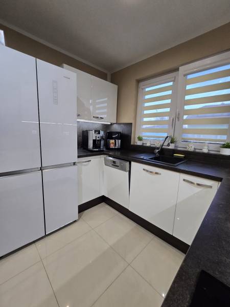 A kitchen in a family house with white cabinets, a black countertop, and cream-colored tiles.