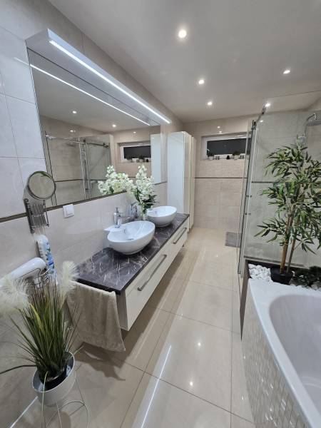 A bathroom in a family house with two sinks, a bathtub, and decorative plants.