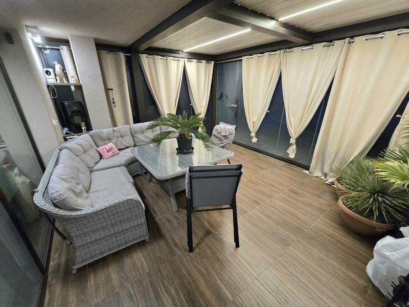 A covered terrace of a family house with a corner sofa and a floor with a wooden decor.