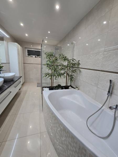 Bathroom with a bathtub, plants, shower, and tiles in a family house.
