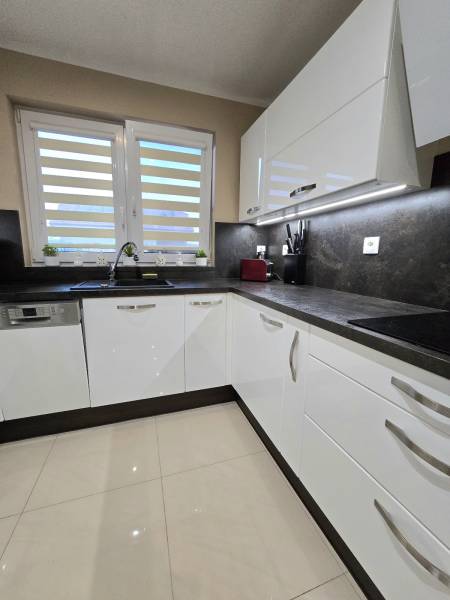 A kitchen in a family house with white cabinets, a dark countertop, and large windows.