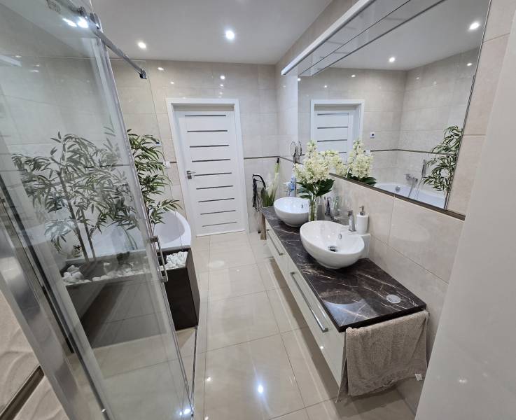 A bathroom in a family house with a modern shower and two sinks on a marble countertop.