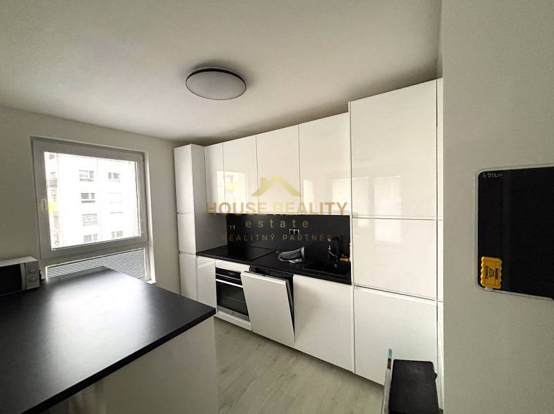 A kitchen with white cabinets, a black countertop, and a window in a 2-room apartment.