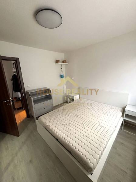 A bedroom in a two-room apartment with a wood-patterned floor and simple furnishings.