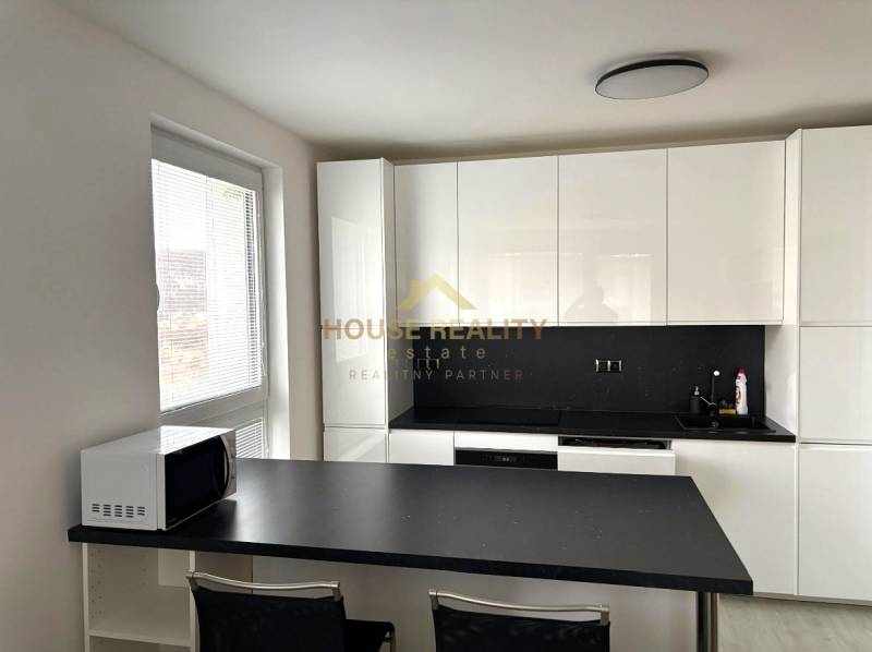 A kitchen in a 2-room apartment with white cabinets and a black countertop.