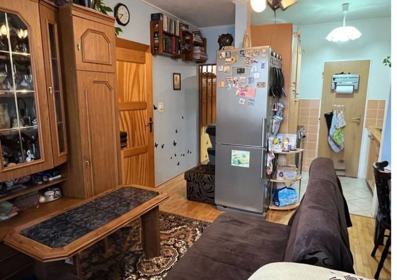 Living room with wood-patterned flooring, seating area, and kitchen.