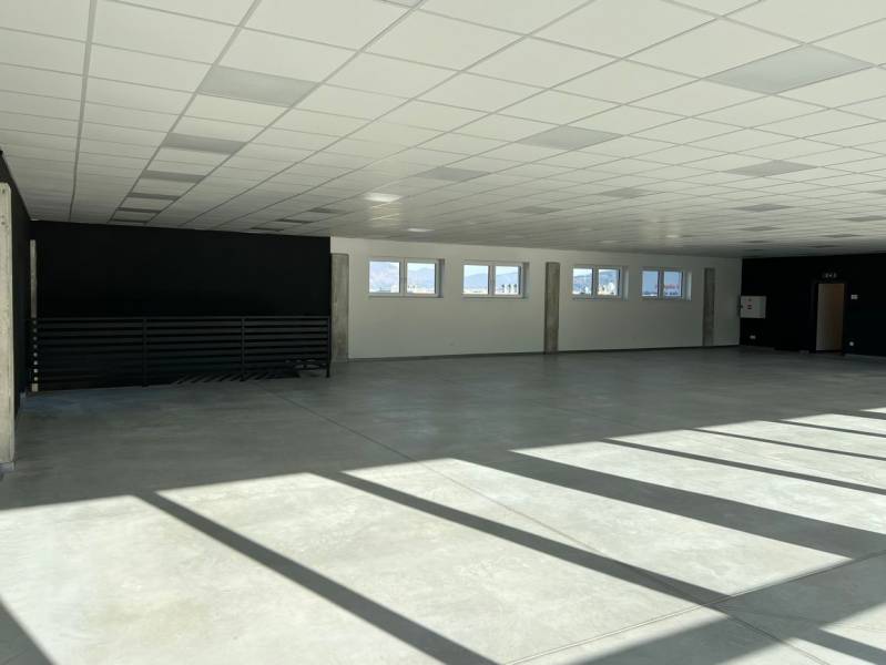 Spacious commercial spaces with concrete flooring and railings, illuminated by windows.