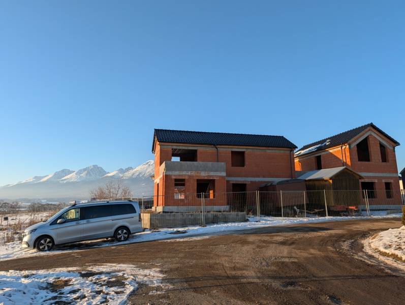 A family house in Mlynica, with snow-covered mountains in the background, a car parked in front.
