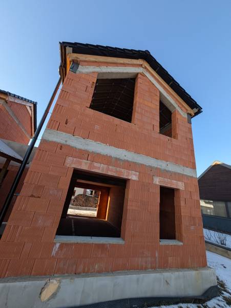 An unfinished family house in the village of Mlynica with red brick walls and a sloped roof.