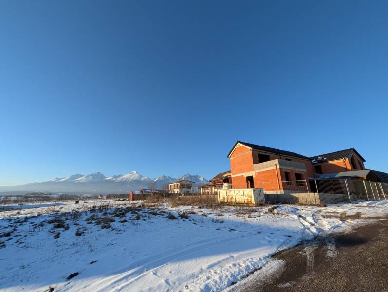 Family houses in Mlynica with snow-covered Tatras in the background under a clear blue sky.
