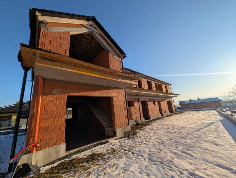 An unfinished family house in Mlynica, surrounded by a snowy landscape and a blue sky.