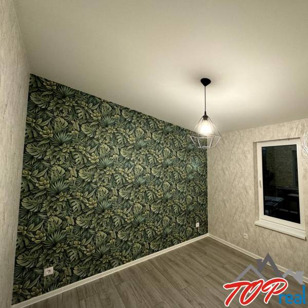 A room in a family house with a wooden decor floor and wallpaper with a tropical pattern.