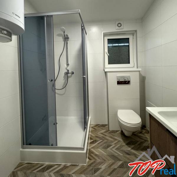 A bathroom in a family house with a modern shower, wooden decor flooring, and white walls.