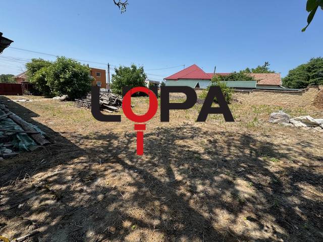 Building plot near a family house in Mužla with a grassy area, trees, and neighboring buildings.