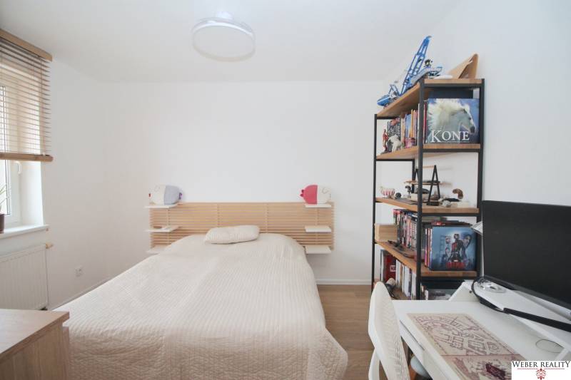 Bedroom in a two-room apartment with a bed, a bookshelf, and wooden floor decor.