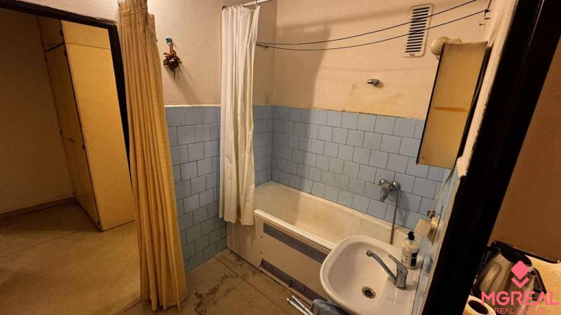 A bathroom with a bathtub and a sink in a 2-room apartment, tiled with light blue tiles.