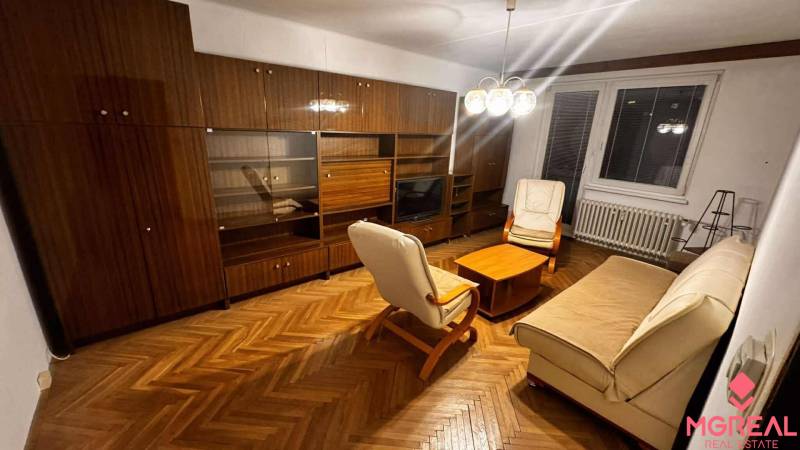 A living room in a two-room apartment with furniture and flooring featuring a wood design.