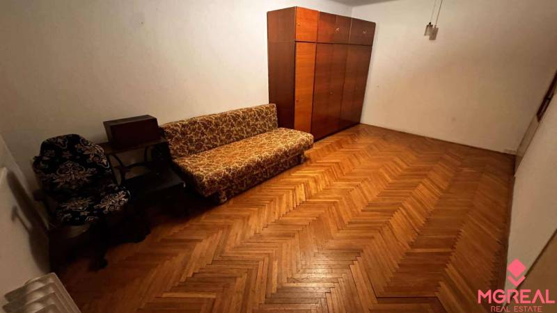A room in a 2-room apartment with a wooden decor floor, a sofa, and a wardrobe.