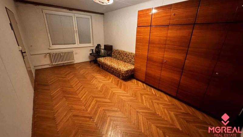 A room in a 2-room apartment with a wooden decor floor, a sofa, and a wardrobe.