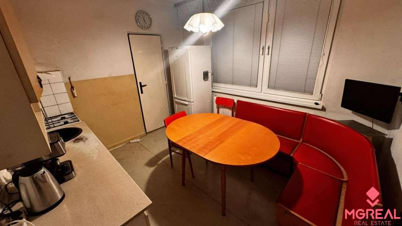 A kitchen in a 2-room apartment with a corner sofa, table, and white kitchen unit.