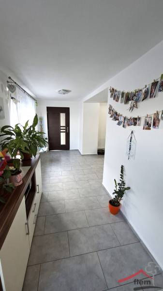 A hallway in a family house with flowers, photographs, and dark doors at the end.
