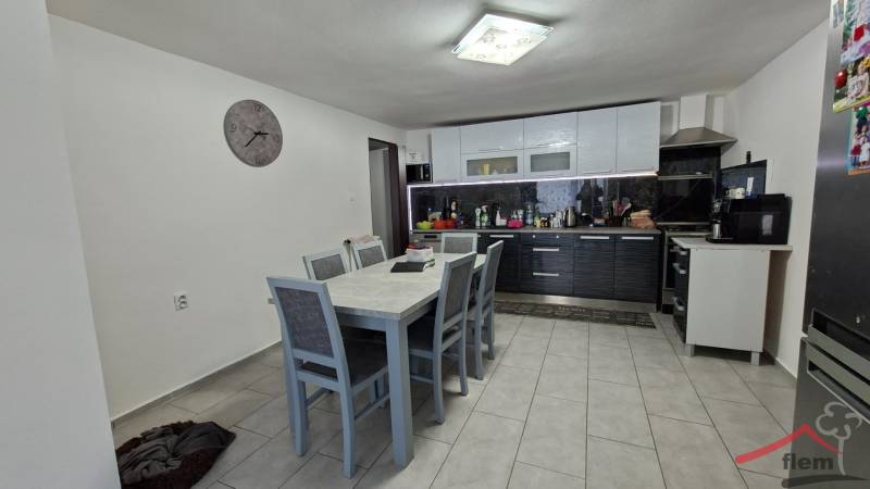 A kitchen in a family house with a dining table, chairs, white furniture, and a wall clock.