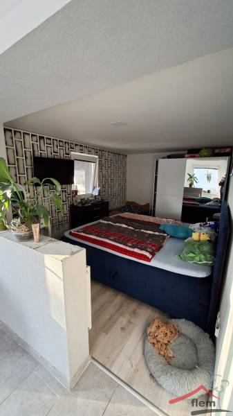 Bedroom with wood-patterned flooring, bed, flowers, and television in a family house.
