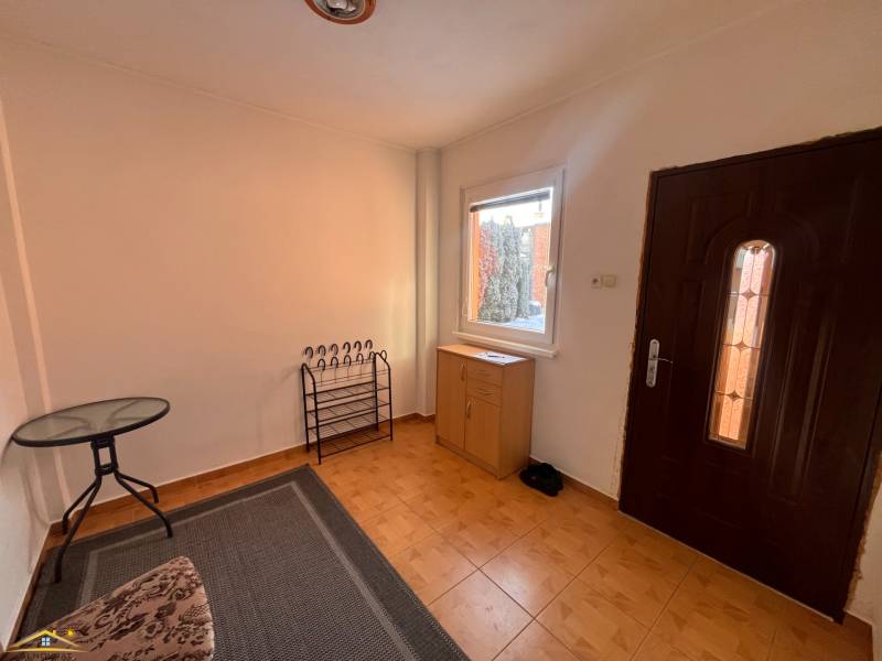Interior of a family house with tiles, a table, a carpet, and a cabinet near the entrance.
