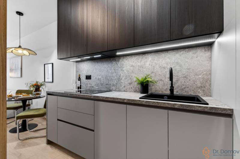 A kitchen in a 2-room apartment with dark cabinets, marble tiles, and a wooden decor floor.