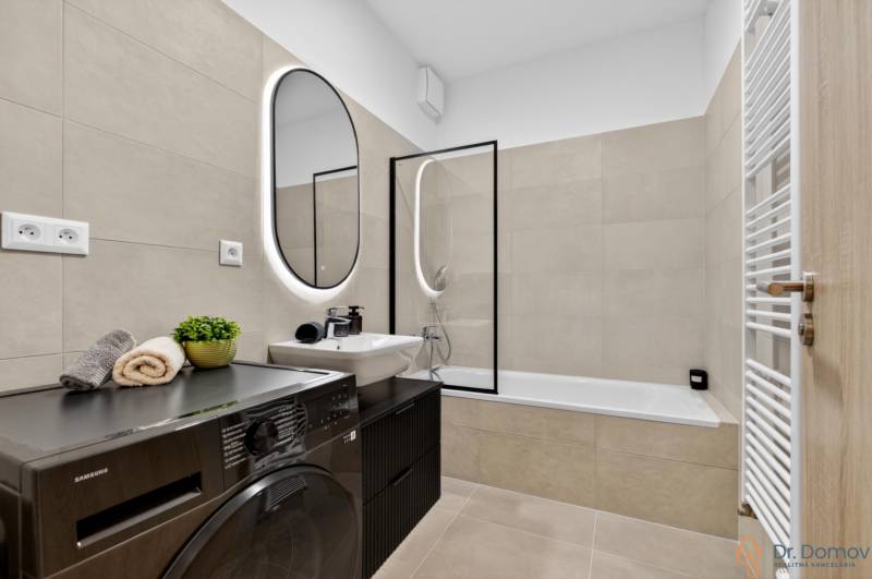 A bathroom in a 2-room apartment with a washing machine, a bathtub, and a mirror with LED lighting.
