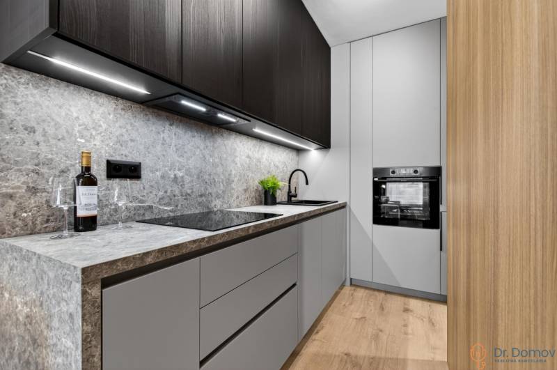 A kitchen with a stone countertop, black cabinets, and a wooden decor floor in a 2-room apartment.