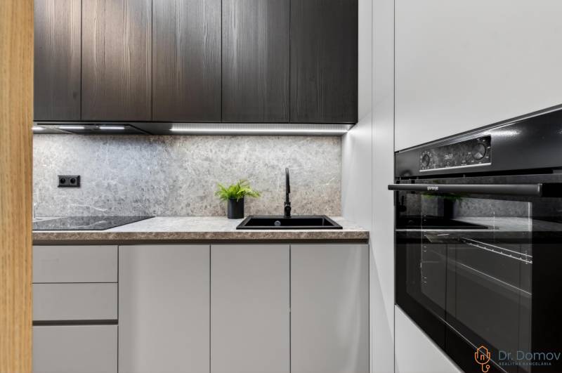 A kitchen in a 2-room apartment with a black oven and a countertop with a stone decor.