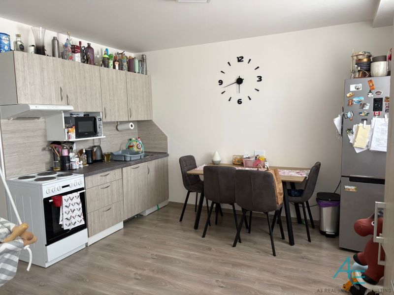 The kitchen of a 2-room apartment with a wooden decor floor, a dining table, and a kitchen unit.