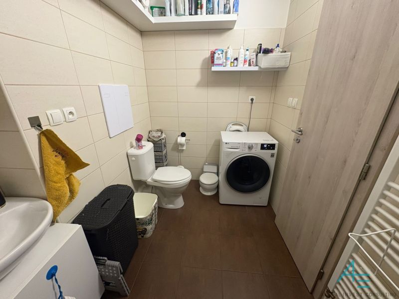Bathroom with a washing machine and toilet in a 2-room apartment, floor with wood decor.