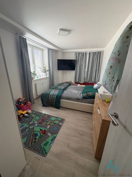 Children's room with a carpet, bed, TV, and floor with wooden decor in a two-room apartment.