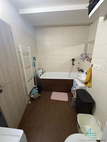 Bathroom in a 2-room apartment with a bathtub, washing machine, and brown floor.