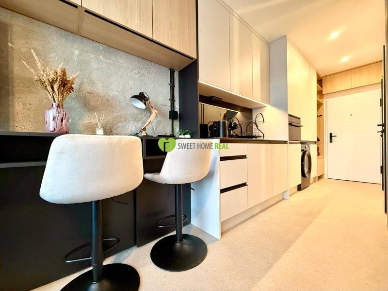 Kitchen corner in a studio apartment with bar stools and modern equipment.