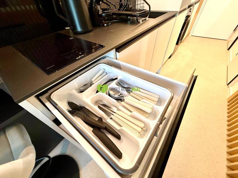 A kitchen in a studio apartment with cutlery in a drawer, a cooktop, and a sink.