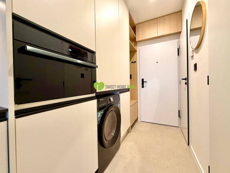 Entrance hallway with a washing machine, built-in oven, and white cabinets in a studio apartment.