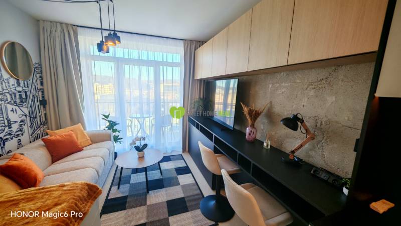 Living room in a one-bedroom apartment with a sofa, a desk, and a view of the balcony.