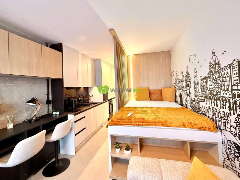 Compact space of a studio apartment with a kitchenette, desk, and bed.