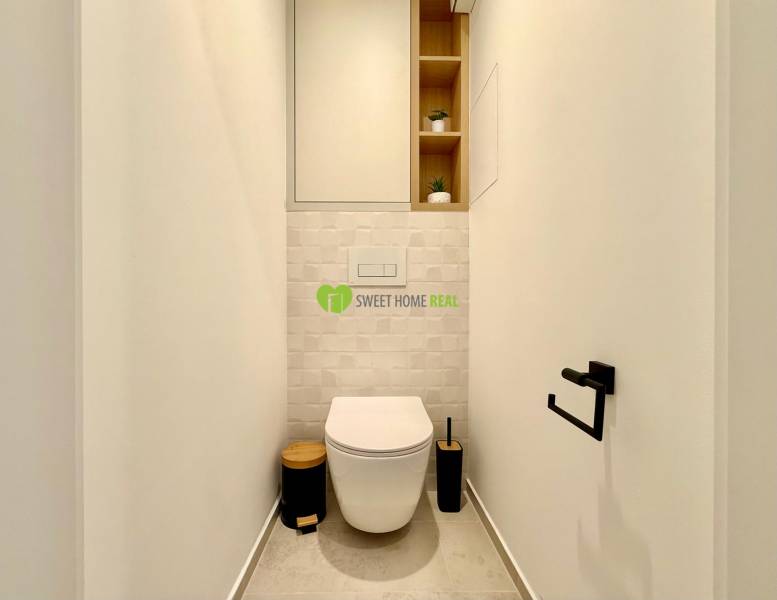 A toilet in a one-room apartment with white walls and built-in shelves.