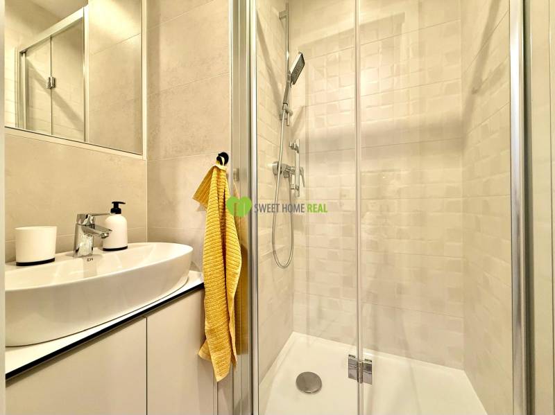 Bathroom in a studio apartment with a white sink, shower stall, and yellow towel.